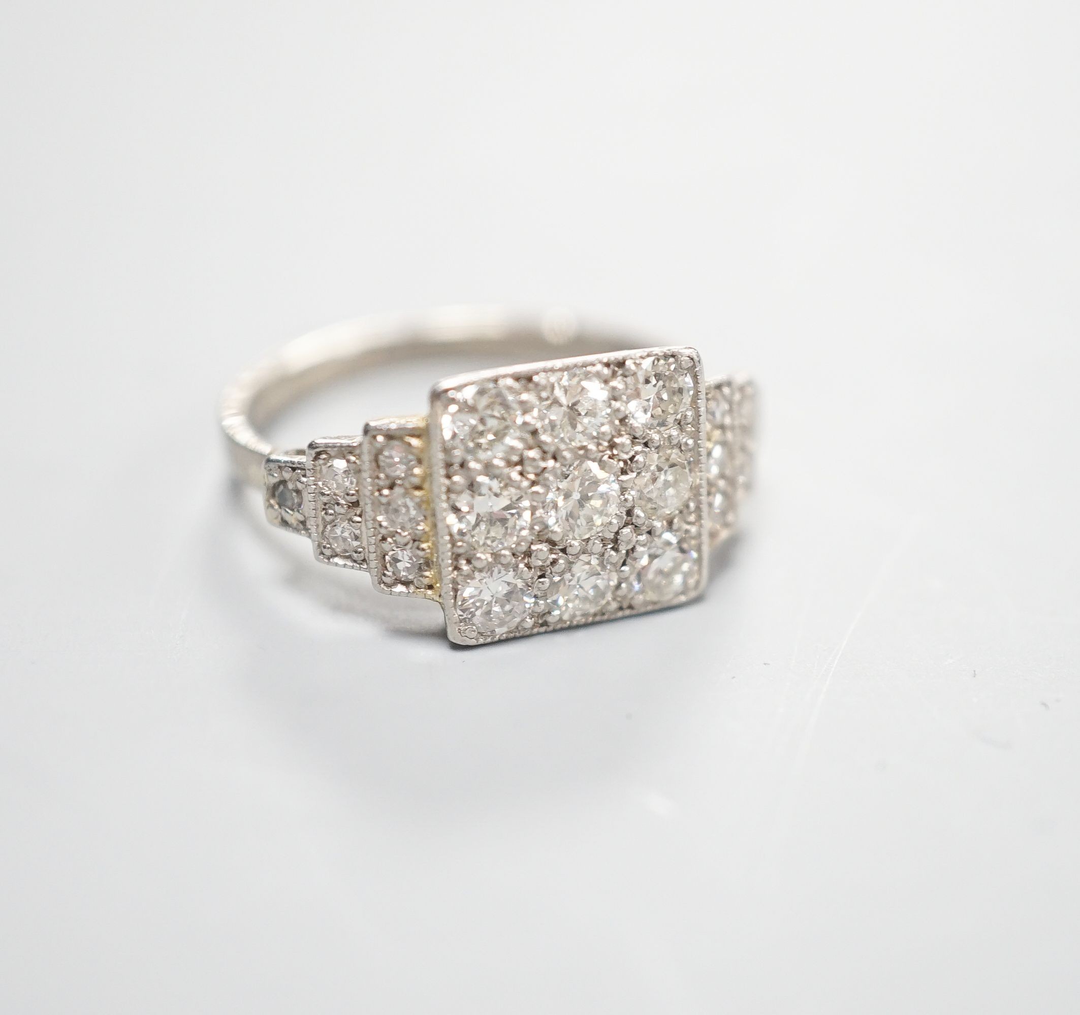 An Art Deco style white metal and nine stone diamond set tablet ring, with diamond set stepped shoulders, size K, gross weight 3.2 grams.